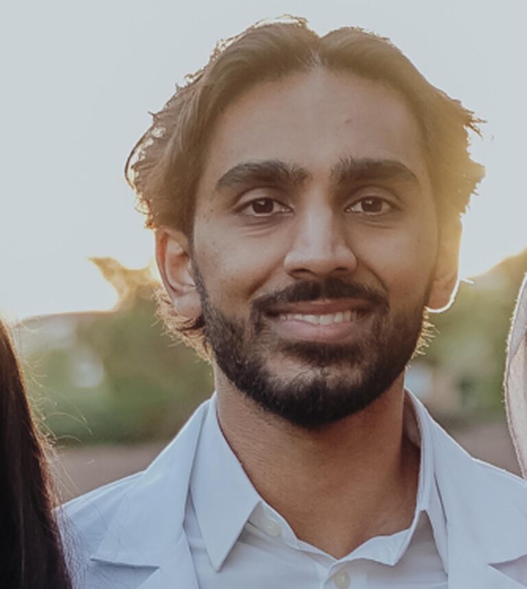 Close-up of a bearded man smiling warmly. Neutral background emphasizes facial expression.
